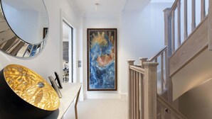 A hallway with a modern interior design, including a round mirror, a large abstract painting, and a wooden staircase.