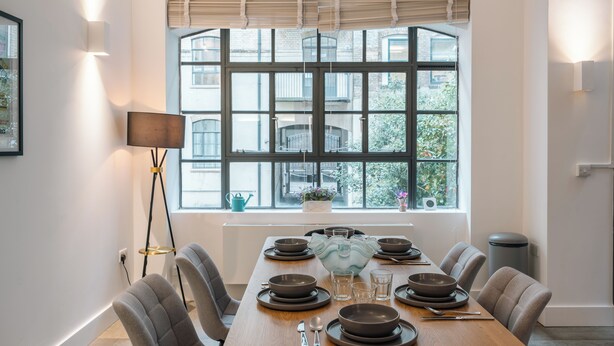 Un comedor con un gran ventanal, una mesa dispuesta con platos y vasos, y una lámpara de pie.