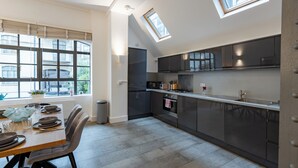 Una cocina moderna con tragaluces, un comedor con mesa dispuesta para cuatro personas y vistas al exterior a través de amplias ventanas.