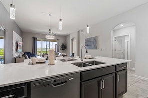 Une cuisine moderne dotée d’un grand îlot central, d’appareils électroménagers intégrés et de luminaires suspendus.