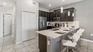 Una cocina moderna con armarios oscuros, un refrigerador de acero inoxidable, un microondas y una isla grande con taburetes de bar.