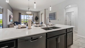 Una cocina moderna con una isla grande, electrodomésticos de acero inoxidable e iluminación colgante.