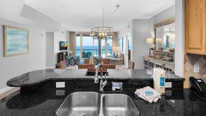A modern kitchen with a large island, double sink, and a view to the living area.