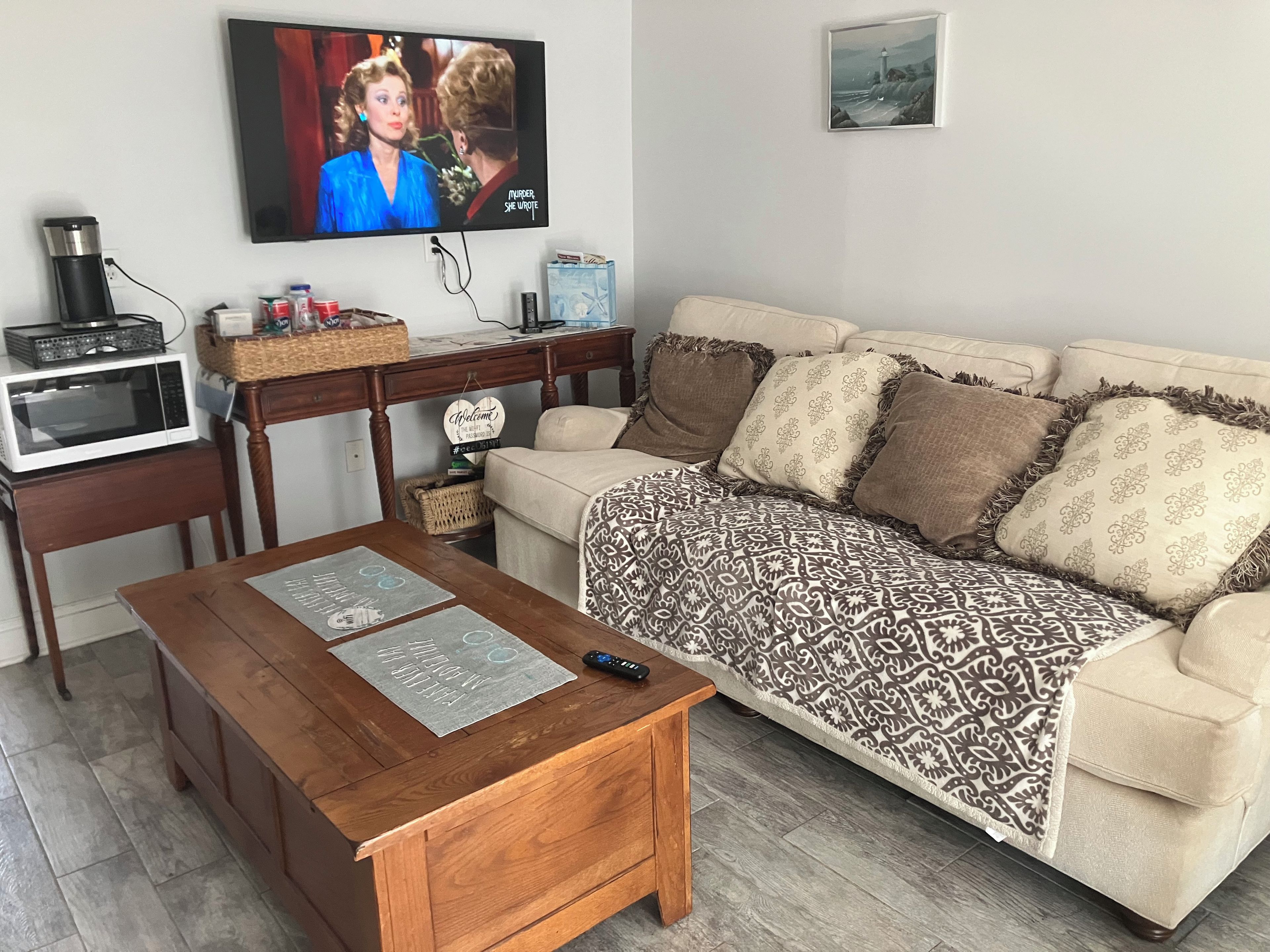 A living room with a television, a wooden coffee table, a beige sofa, and a patterned throw blanket.