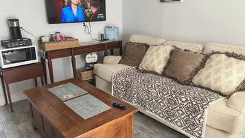 A living room with a television, a wooden coffee table, a beige sofa, and a patterned throw blanket.