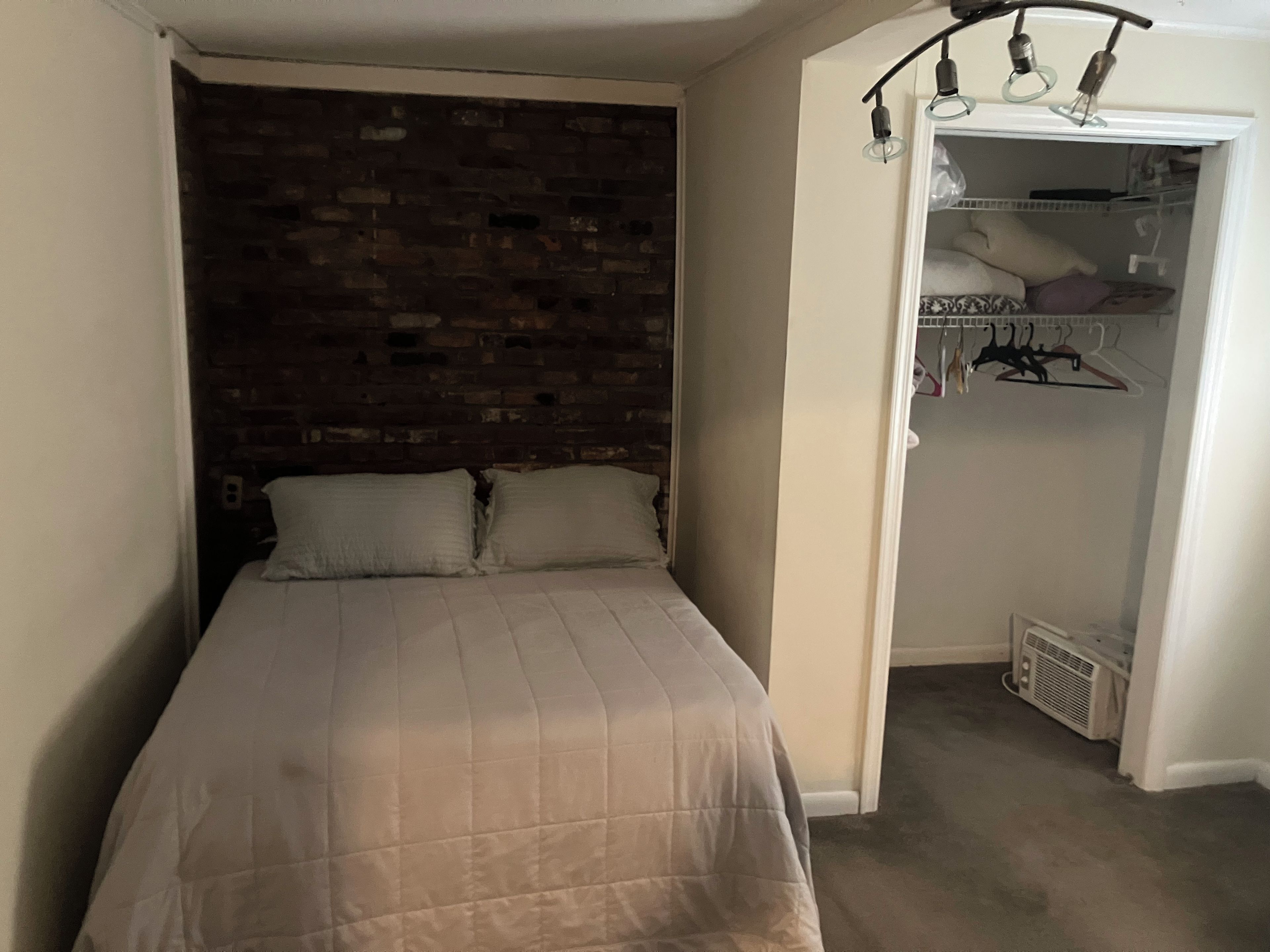 A bedroom with a bed, a brick wall, and a closet with hanging clothes.