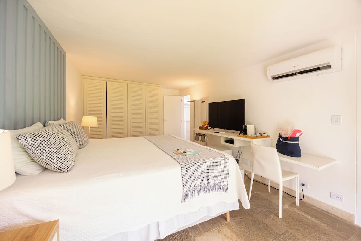 Une chambre d’hôtel comprenant un lit, une table de chevet, une lampe, un bureau, une chaise, un téléviseur, un climatiseur et un placard.