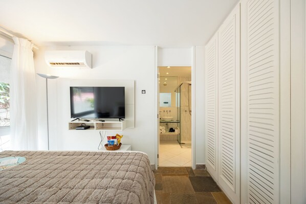 A bedroom with a bed, a TV, a TV stand, a basket, and a door leading to a bathroom.