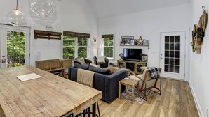 Ein geräumiges Wohnzimmer mit einem großen Holztisch, dunklen Sofas, einem Fernseher und einem Kamin.