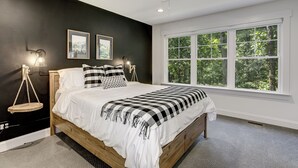 Ein Schlafzimmer mit großem Fenster, Deckenventilator und einem Bett mit schwarz-weiß kariertem Überwurf.