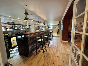 A bar area with wooden flooring, bar stools, a counter with a wooden top, and hanging pendant lights. - Orø Kro & Hotel (Orø)