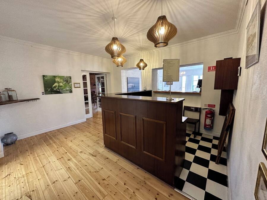 A hotel lobby with a wooden reception desk, pendant lighting, a checkered floor, and a fire extinguisher.