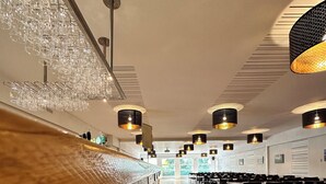 Un restaurante amplio con suelo de madera, mesas altas y lámparas colgantes.