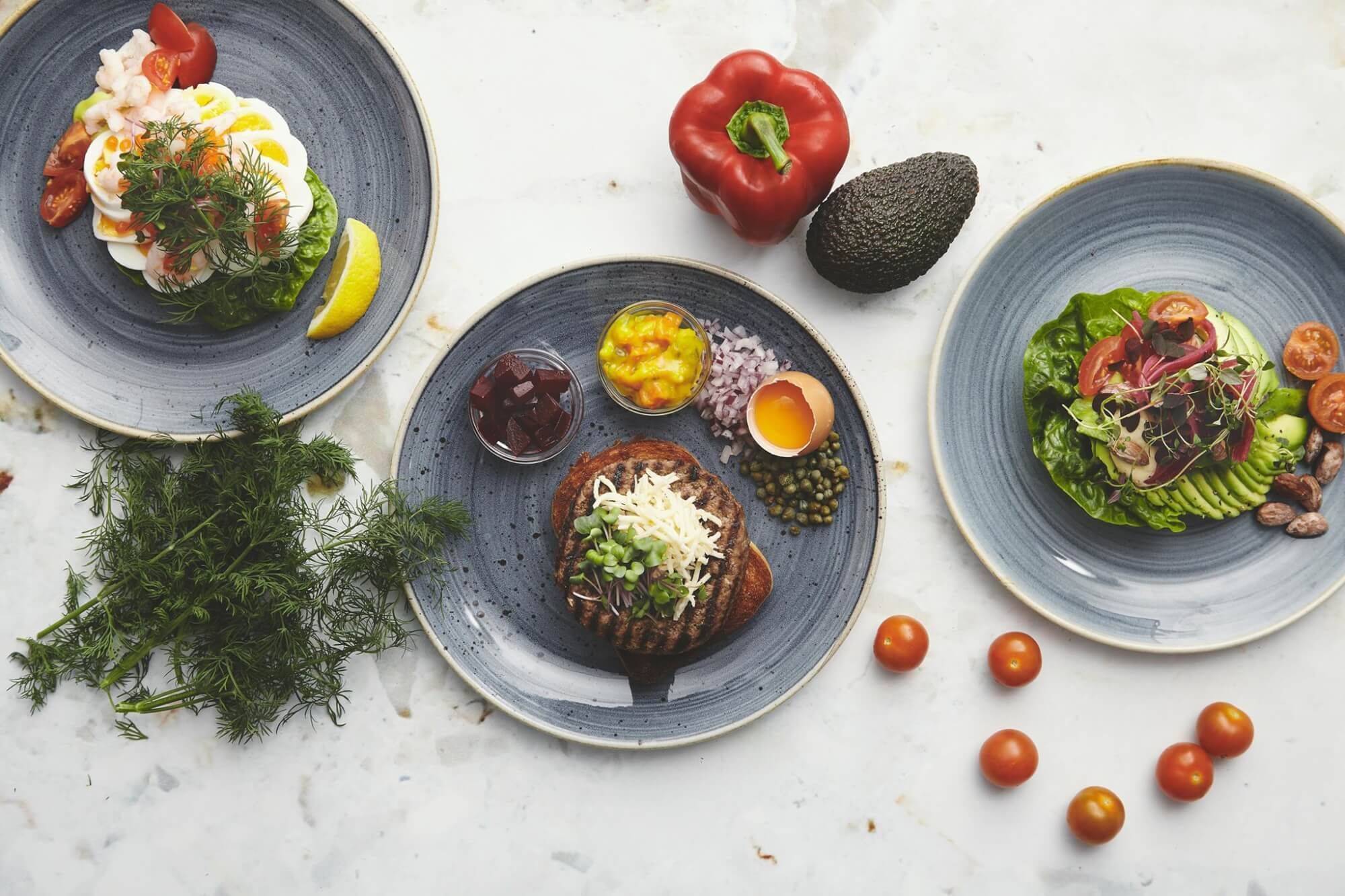 Three plates of food with various vegetables and a whole avocado.