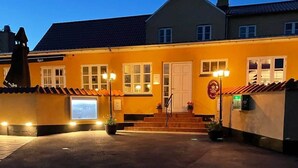 Un edificio de dos pisos con fachada amarilla, una entrada principal con escalones y un estacionamiento al frente.