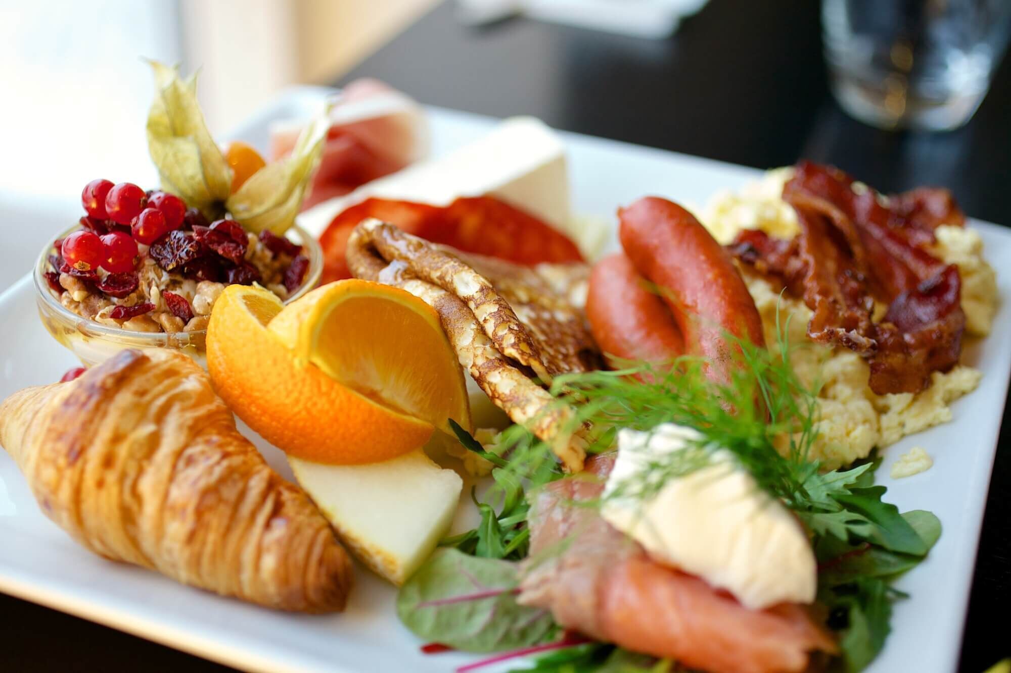 Un plato de desayuno con cruasanes, rodajas de naranja, queso, tocino, salmón y una ensalada.