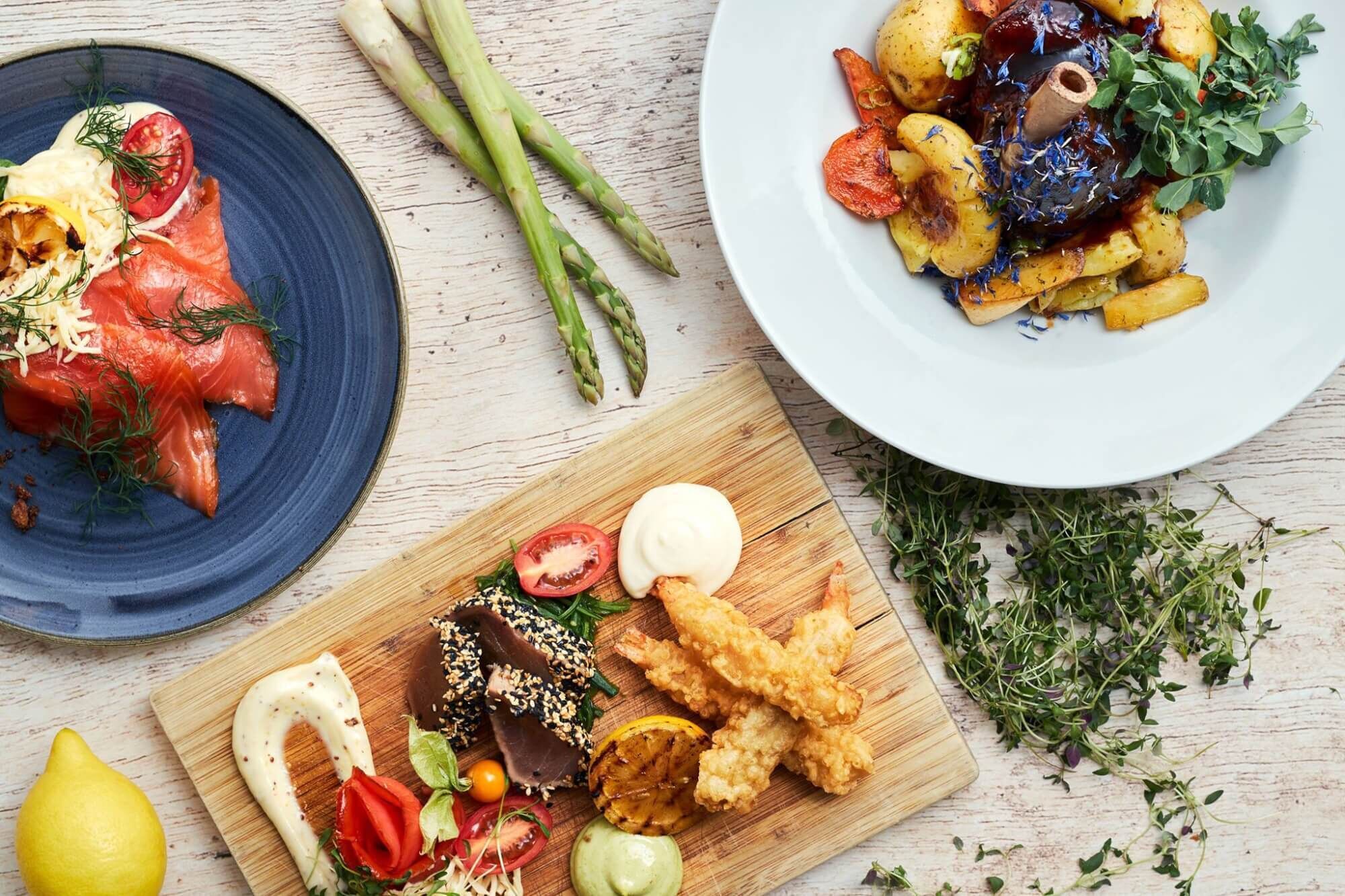 A variety of dishes including smoked salmon, roasted vegetables, and fried items, suggesting a meal setting.