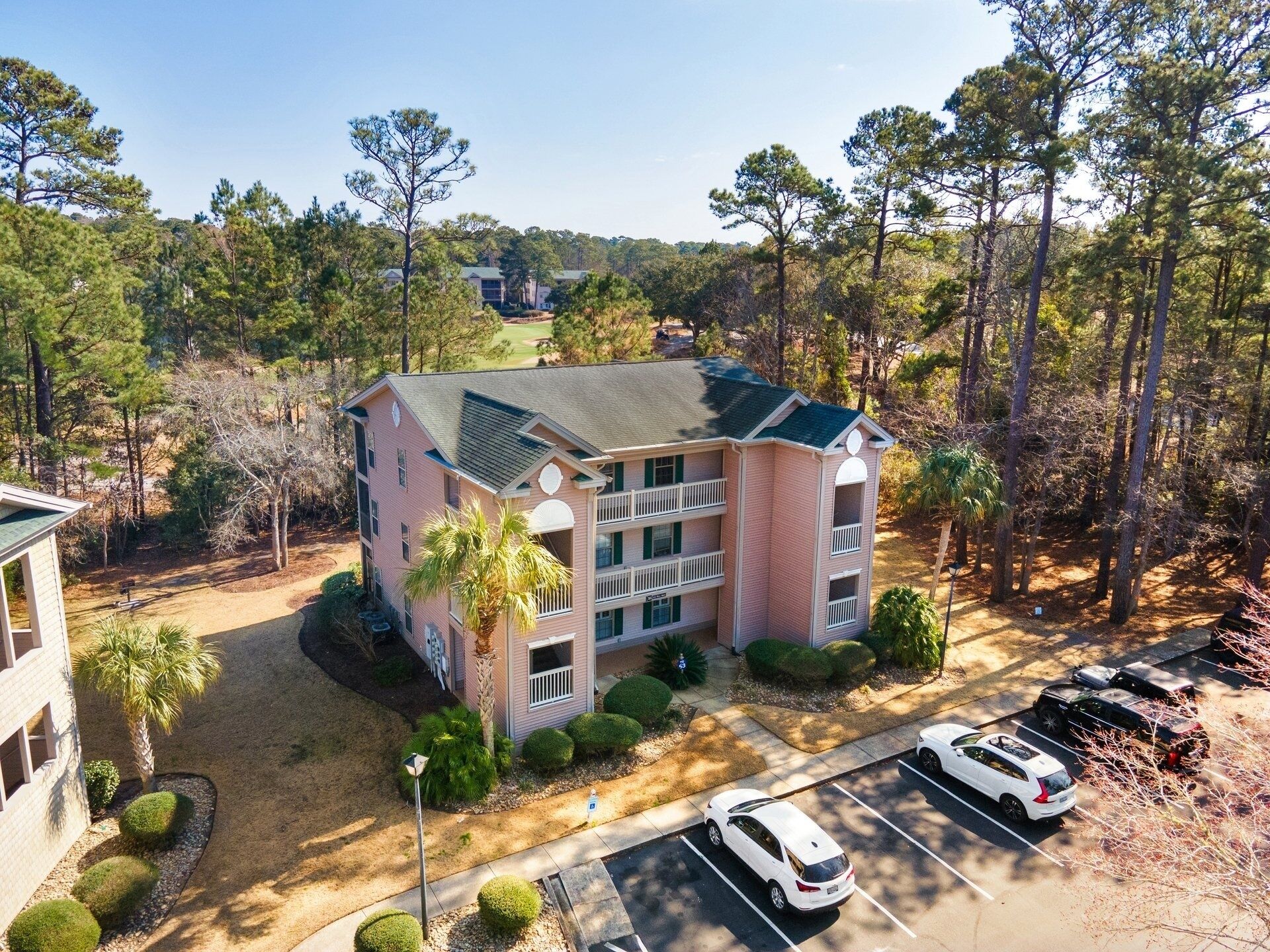 A multi-story building with a flat roof, surrounded by trees and a parking lot.