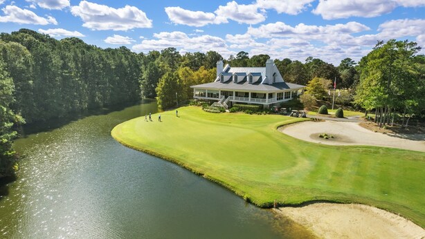 A golf course with a clubhouse, a river, and a forested area.