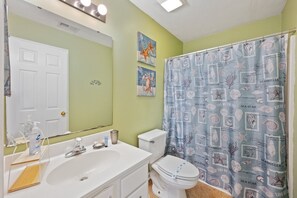 A bathroom with a white sink, toilet, and shower curtain with seashells and starfish design.