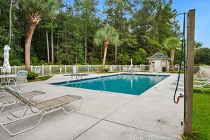 A swimming pool with lounge chairs, a lifeguard station, and a small building in a wooded area.