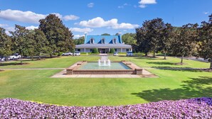 A large building with a blue roof, a central fountain, and a well-maintained lawn with purple flowers.