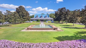 A large building with a blue roof, a central fountain, and a well-maintained lawn with purple flowers.