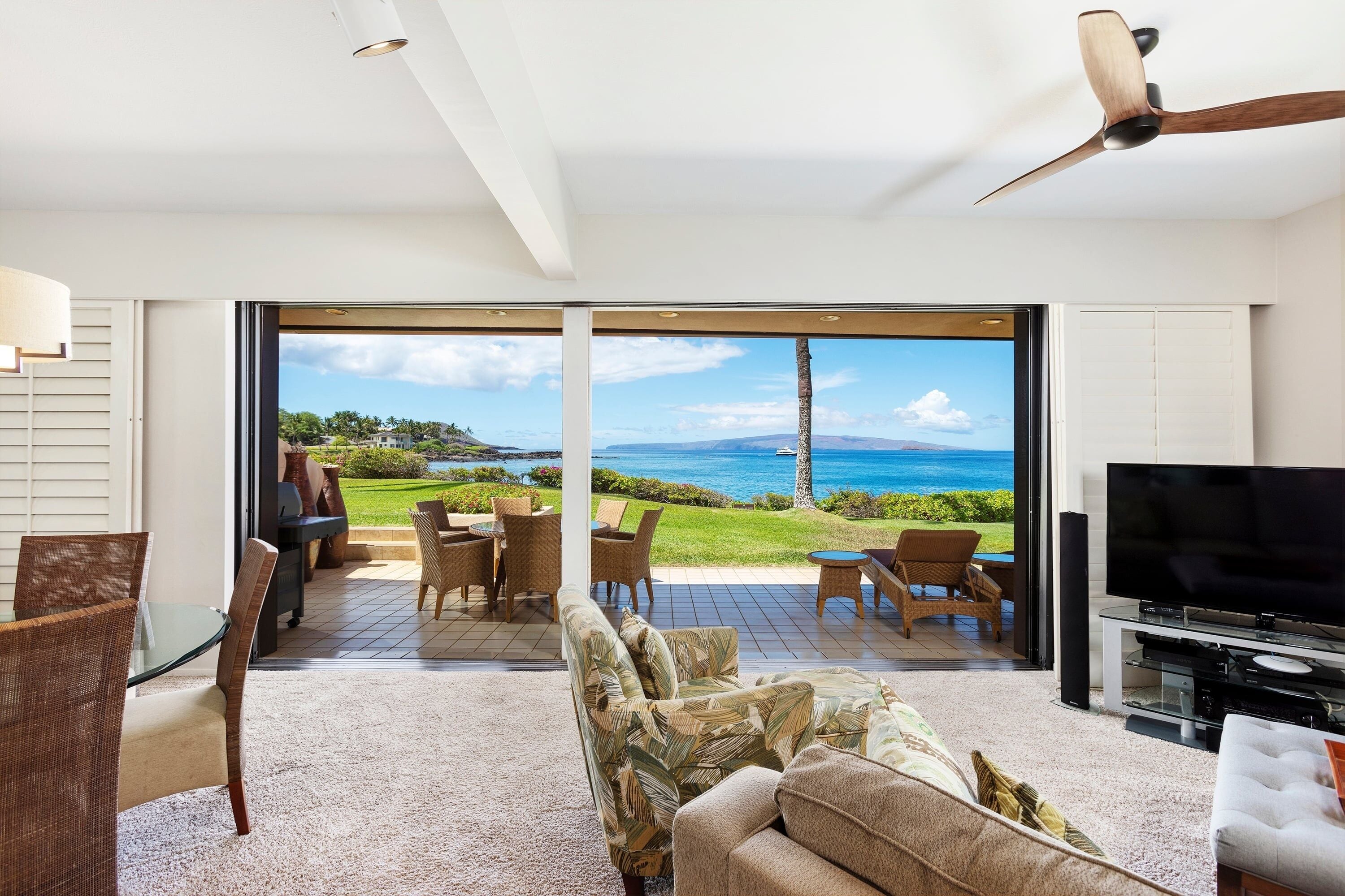 Uma sala de estar moderna com uma televisão grande, assentos confortáveis e vista para o mar.