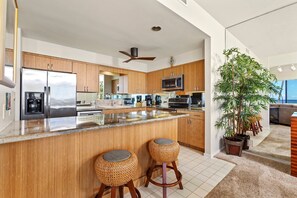 A modern kitchen with a central island, stainless steel appliances, wooden cabinets, and a ceiling fan.