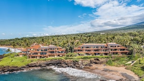 Um resort costeiro com vários edifícios, uma praia e montanhas ao fundo.