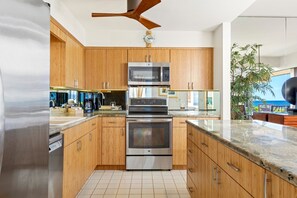 A modern kitchen with wooden cabinets, stainless steel appliances, and a view of the ocean. - Makena Surf, #f-104 3 Bedroom Condo (Kihei)