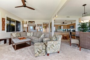 A spacious living room with a large sofa, a coffee table, and a patterned armchair. There is a kitchen area with a bar and a dining table. - Makena Surf, #f-104 3 Bedroom Condo (Kihei)