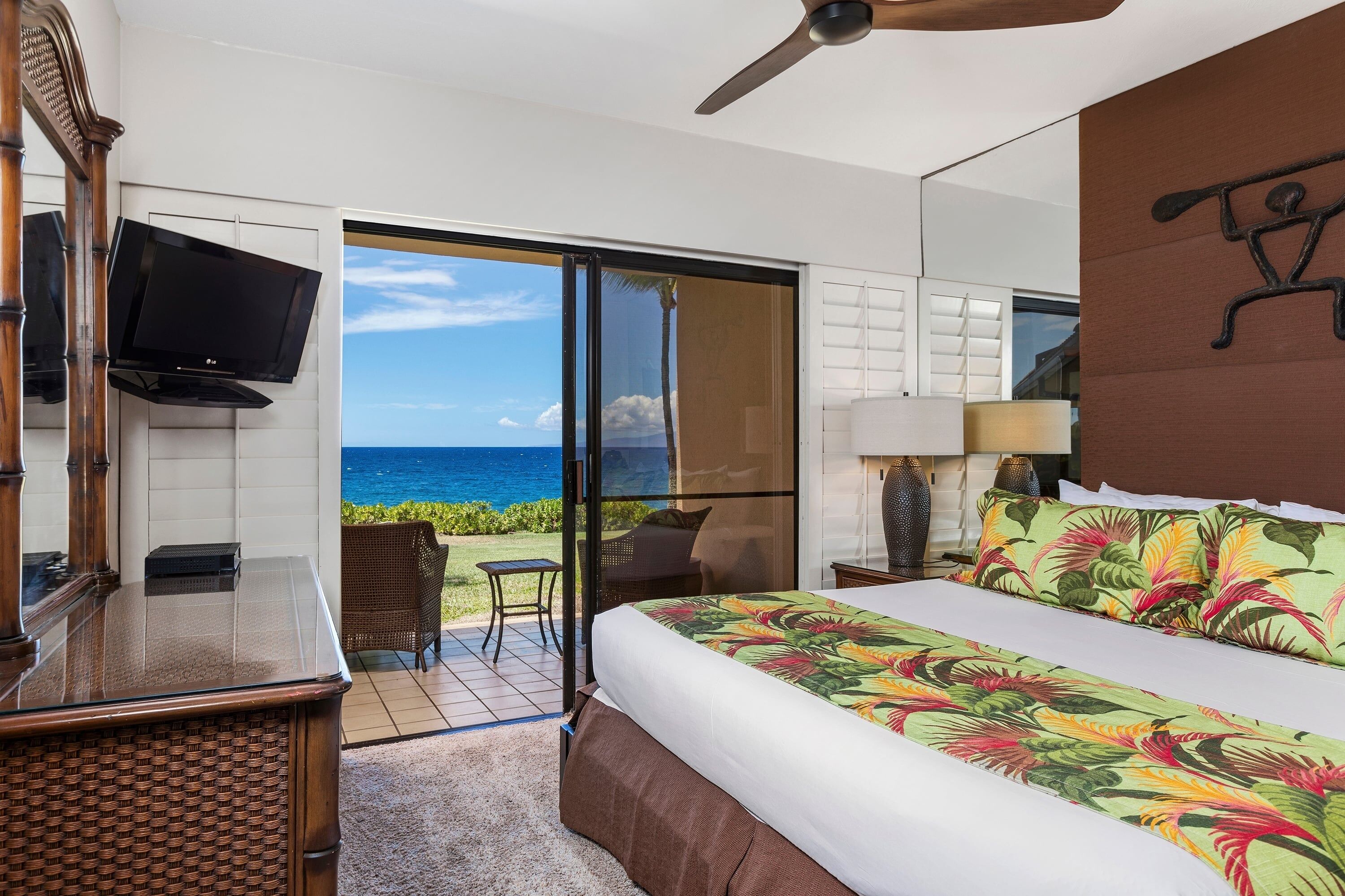 Quarto de hotel com cama, televisão, varanda e vista para o oceano, e ventilador de teto.