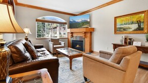 A cozy living room with a fireplace, leather sofa, armchair, and a large window offering a scenic view. - Villa 2082 2 Bed 2 Bath Full Kitchen 2 Bedroom Villa (Midway)