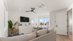 Ein modernes Wohnzimmer mit einer Couch, einem Esstisch, Stühlen, einem Fernseher und einem Deckenventilator.