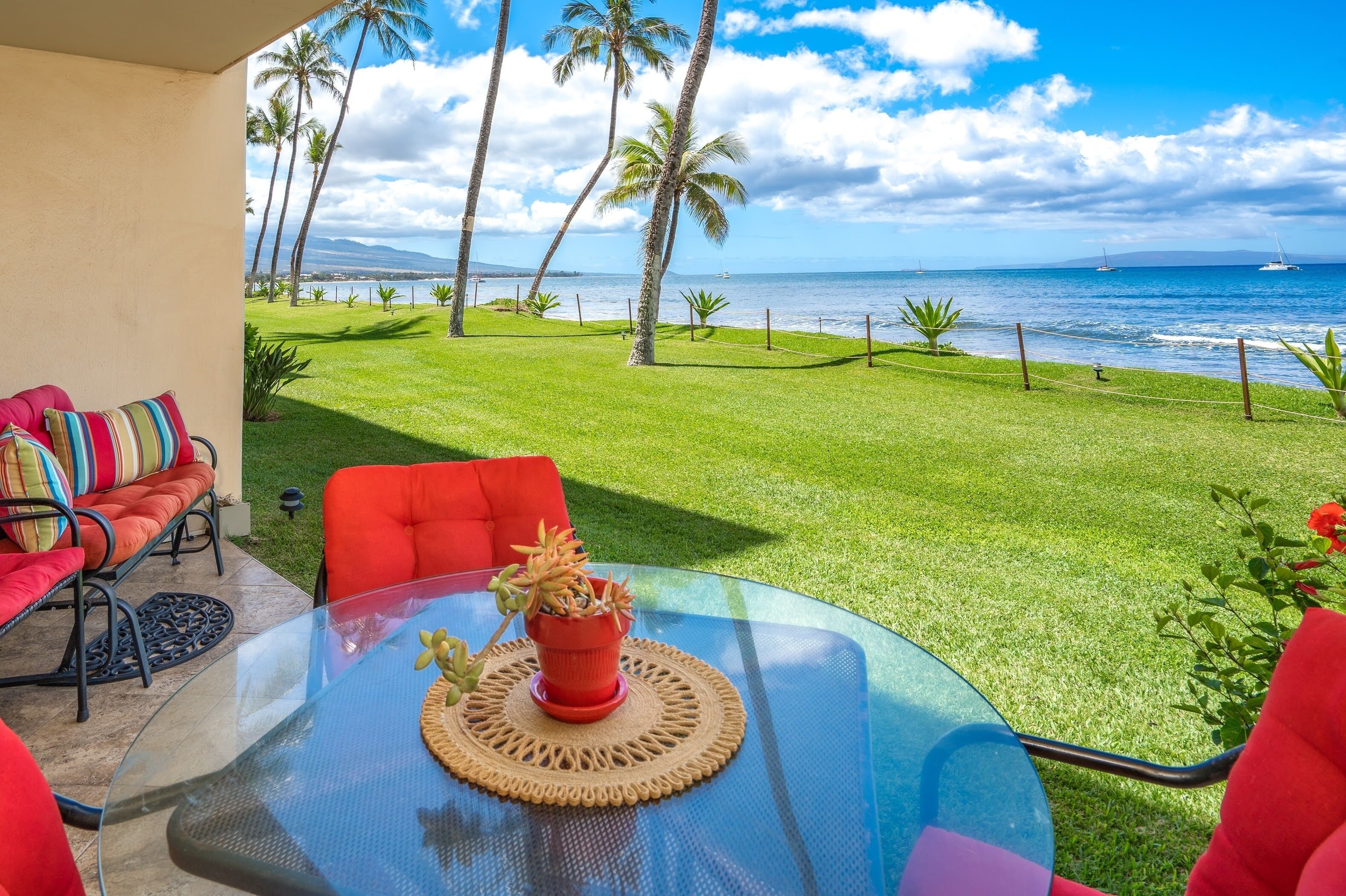 A glass table with a woven placemat, red chairs, and a colorful sofa with striped cushions.