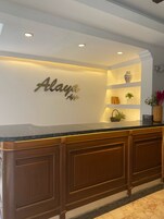 A reception desk with a marble countertop, wooden cabinets, and a wall-mounted sign that reads "Alaya."