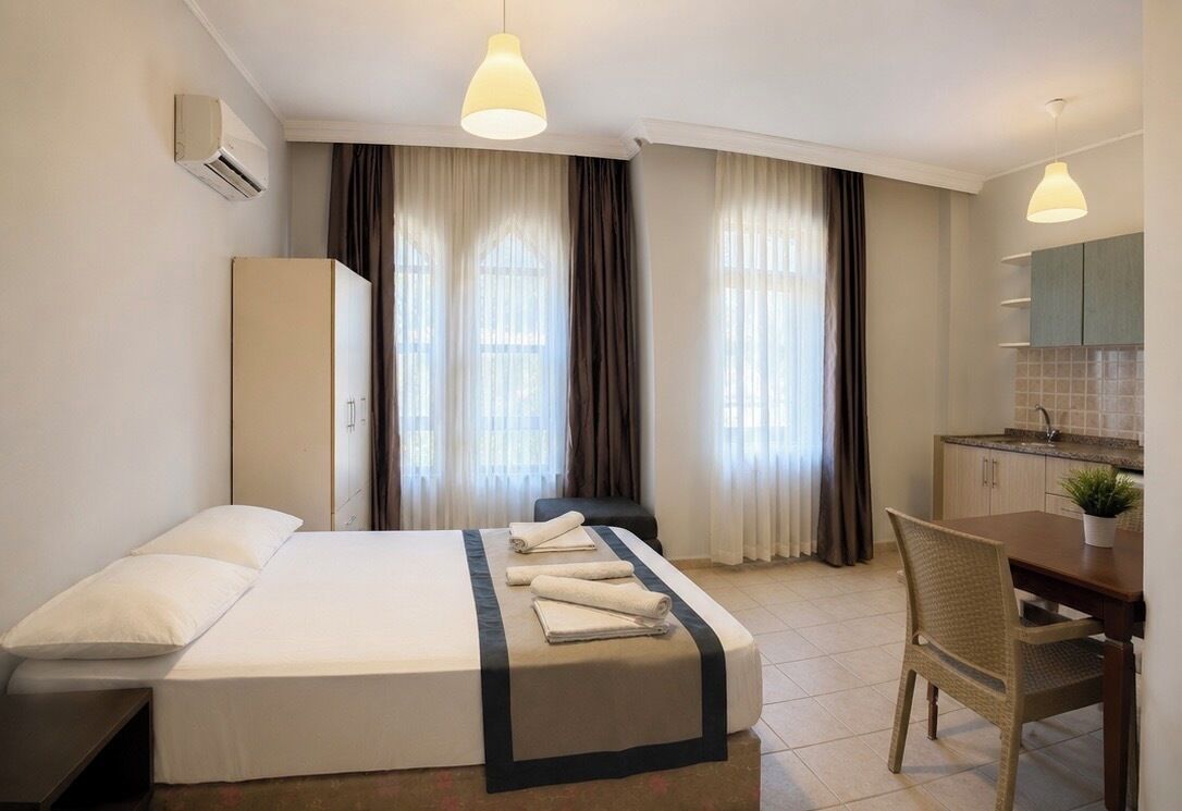 Una habitación de hotel con cama, escritorio, silla, kitchenette y cortinas.