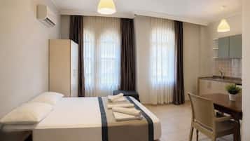 A hotel room with a bed, a desk, a chair, a kitchenette, and curtains.