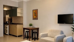 A modern hotel room with a bed, two armchairs, a dining table with stools, a kitchen area, and a TV mounted on the wall. - Alaya Apart Otel (Alanya)