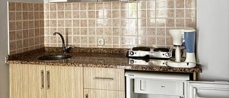 A compact kitchen with a sink, countertop, cabinets, a small refrigerator, and a hanging light fixture.