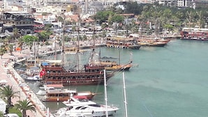 A marina with various boats docked, including a large ship with a red flag. - Alaya Apart Otel (Alanya)