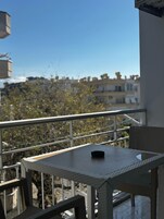 A balcony with a table and chairs, overlooking a residential area with trees and buildings.