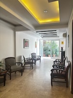 A spacious lobby with a modern ceiling design, a seating area with chairs and a table, and a view of the outdoors through large glass doors.