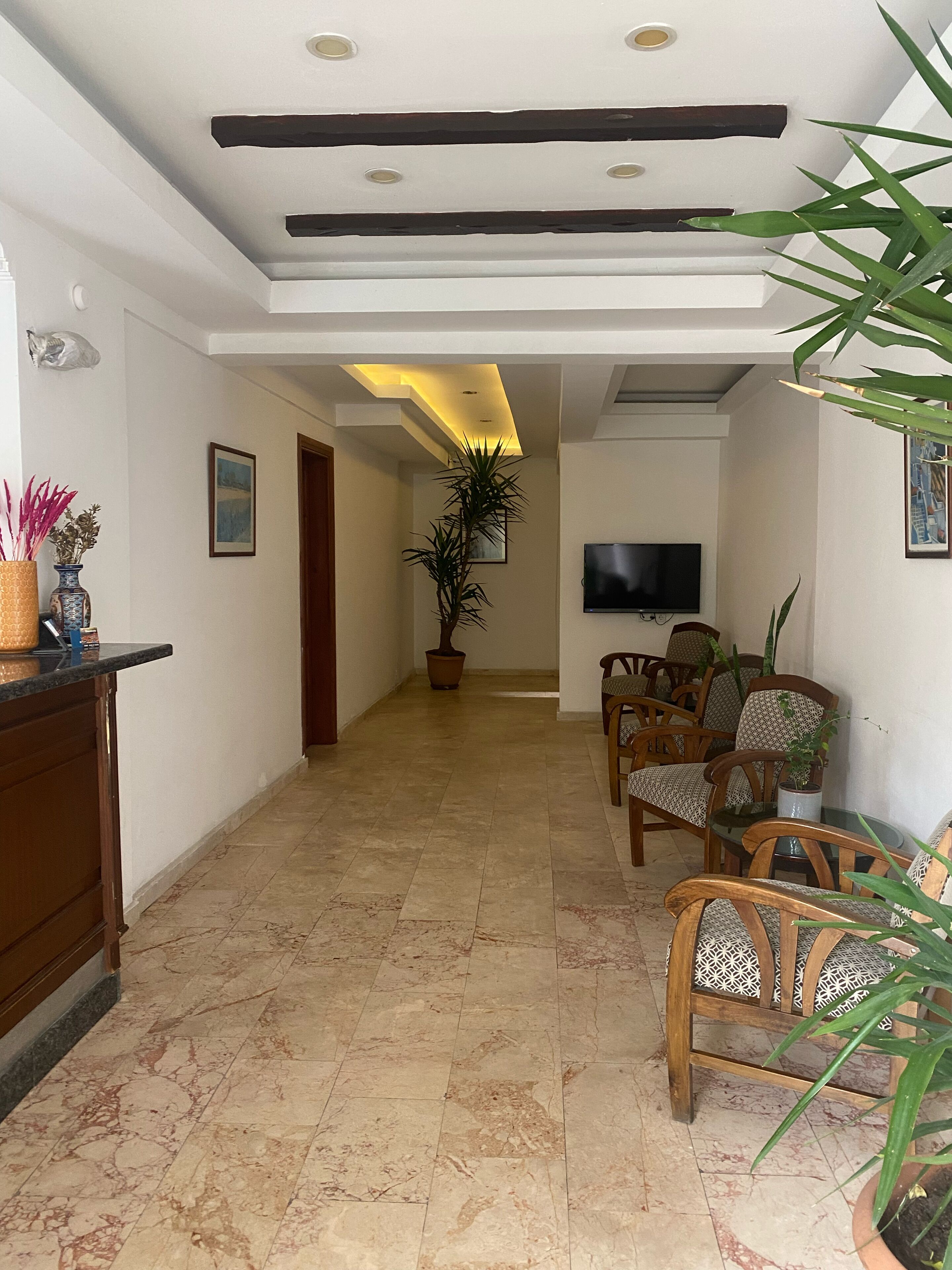 A spacious living area with a high ceiling, a flat-screen TV mounted on the wall, and a dining area with wooden chairs and a glass table.
