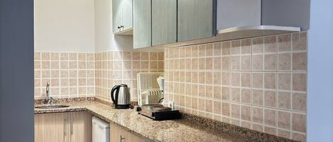 A kitchen with light wood cabinets, a granite countertop, a coffee maker, and a kettle.