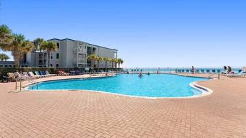 A swimming pool with lounge chairs, a building with balconies, and a clear sky.