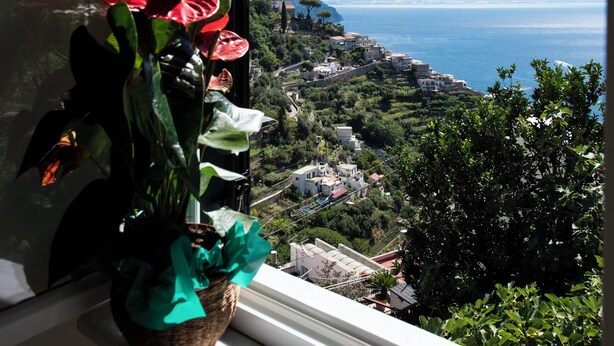 A window with a view of a coastal landscape, including a body of water and distant mountains. - SAM'S HOUSE - A corner of paradise suspended between sky and sea (Amalfi)