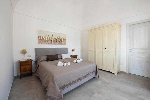 Un dormitorio con cama, mesita de noche, lámpara, armario y un cuadro en la pared.