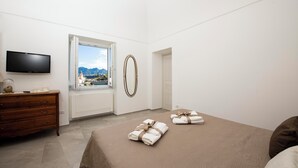 A hotel room with a bed, a dresser, a TV, a window with a view, and a towel rack. - SAM'S HOUSE - A corner of paradise suspended between sky and sea (Amalfi)